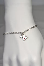 handmade silver heart bracelet by Christine Sadler. Two hearts hang at the front, one larger than the other. The larger heart is matt finished and set with a ruby gemstone