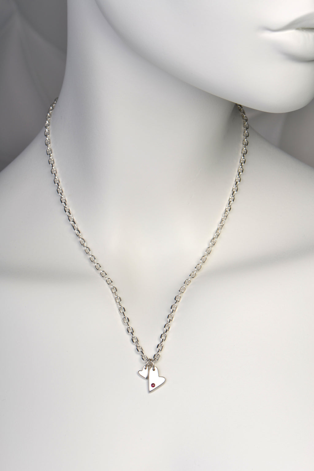 Sterling silver double heart necklace set with a ruby from the From The Heart collection by Christine Sadler shown on a white mannequin to show size and scale

