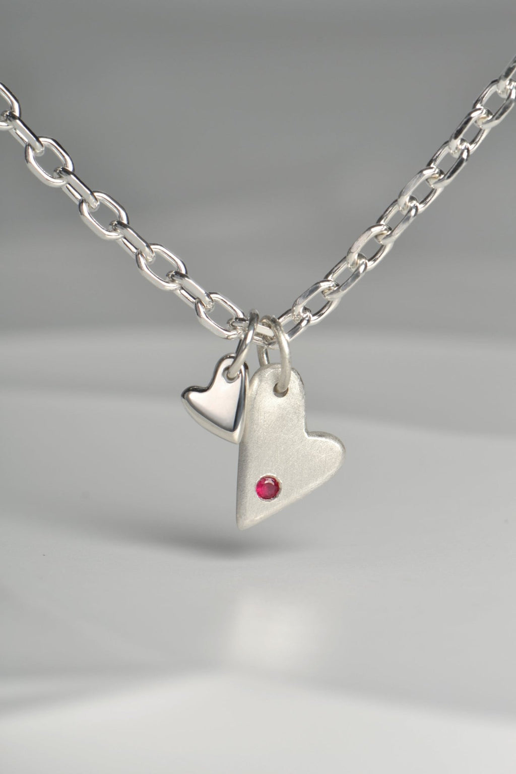 close up of sterling silver double heart necklace set with a ruby displayed on white background from the From The Heart collection by Christine Sadler

