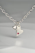 close up of sterling silver double heart necklace set with a ruby displayed on white background from the From The Heart collection by Christine Sadler

