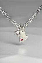 close up of sterling silver double heart necklace set with a ruby displayed on white background from the From The Heart collection by Christine Sadler


