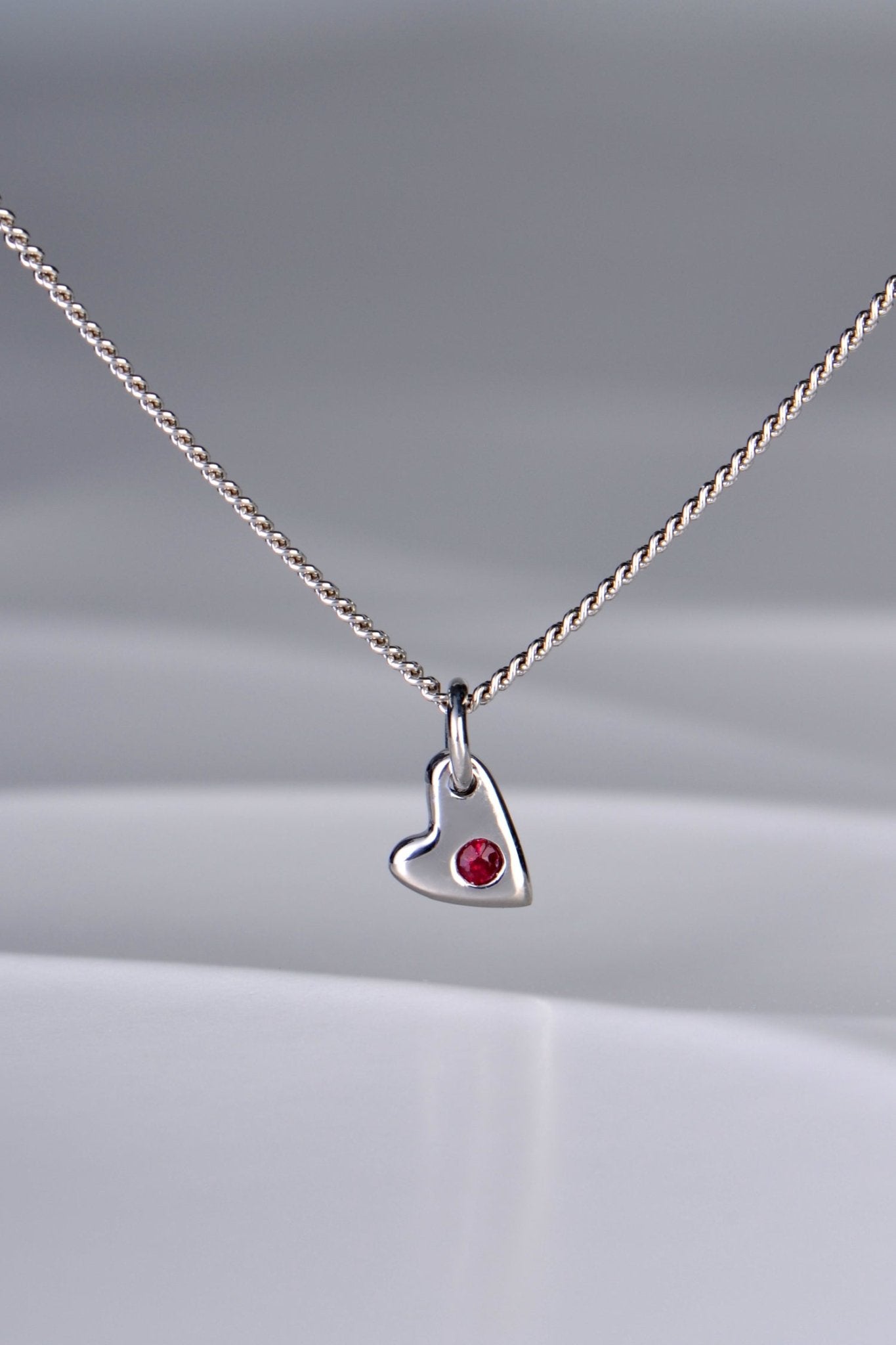 Small polished white gold heart necklace with a ruby displayed on white background from the From The Heart collection by Christine Sadler