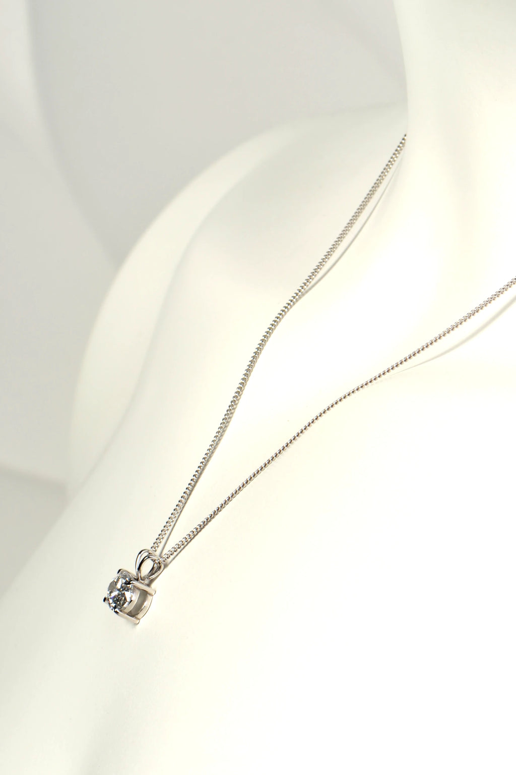 Side view of a white gold diamond pendant showing the double bail design, talon claws, and low-profile basket setting. Christine Sadler