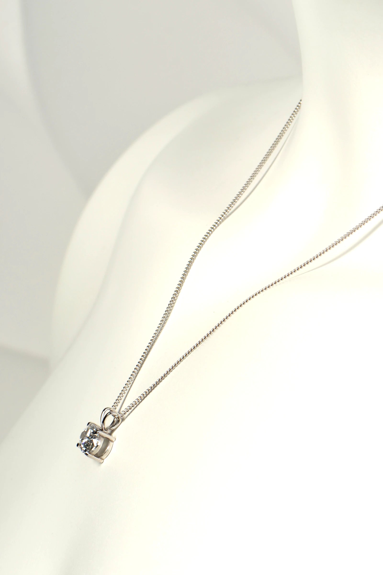 Side view of a white gold diamond pendant showing the double bail design, talon claws, and low-profile basket setting. Christine Sadler
