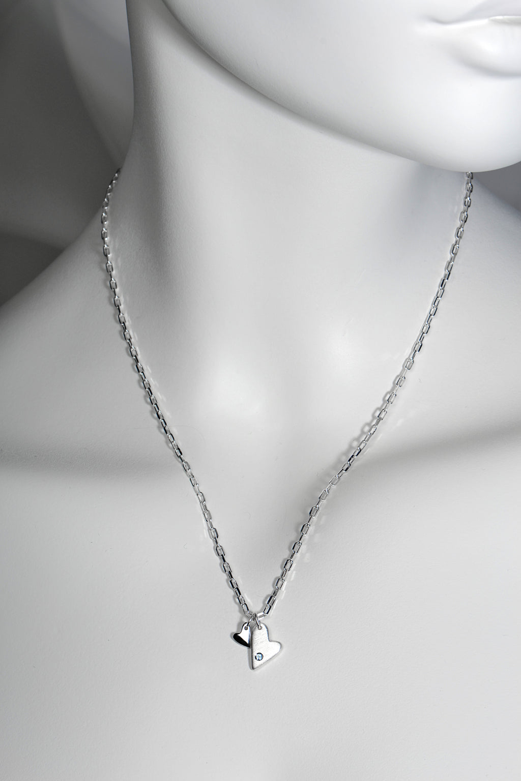Sterling silver double heart necklace set with aquamarine displayed on white mannequin to show size and scale. 