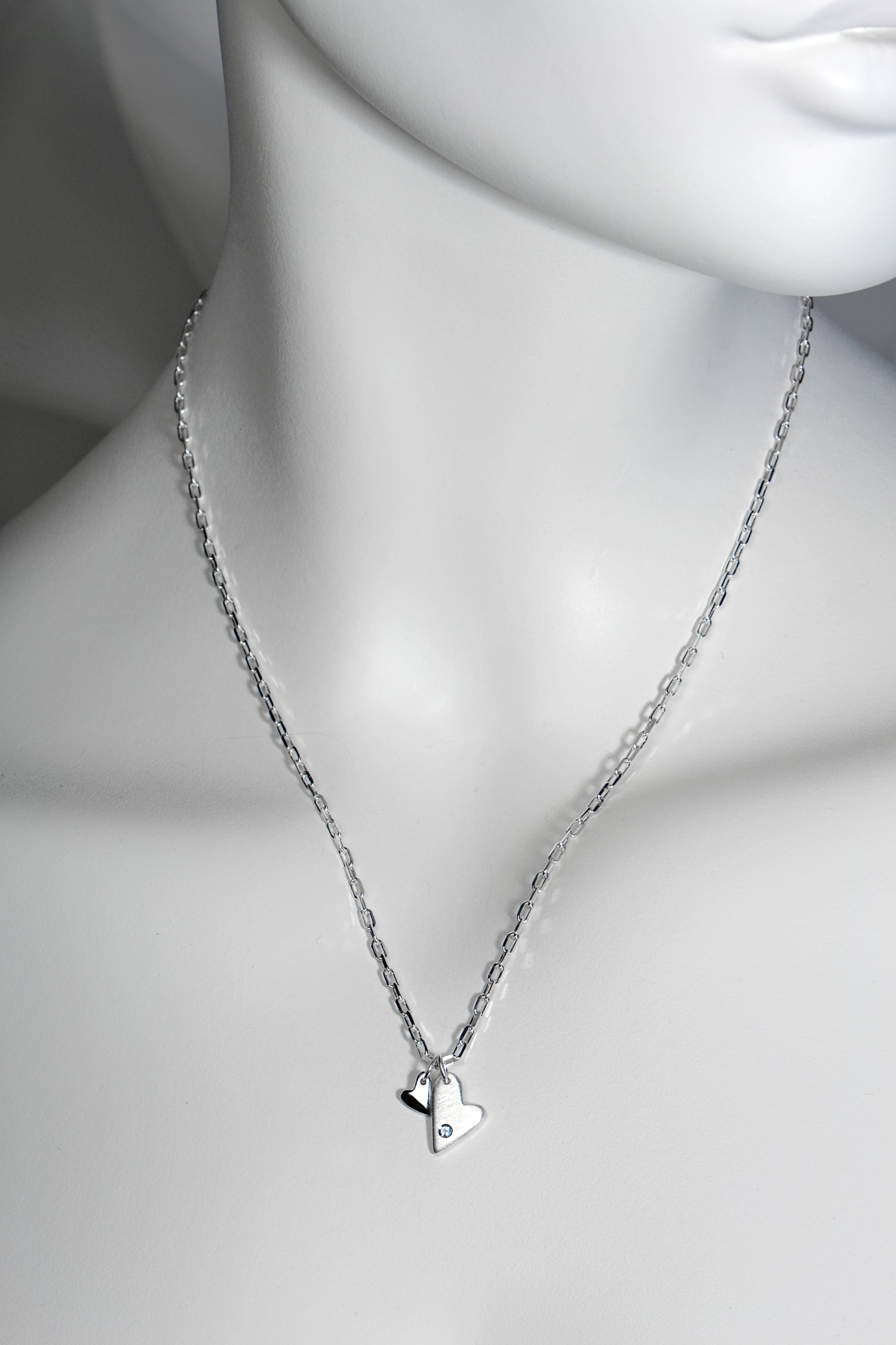 Sterling silver double heart necklace set with aquamarine displayed on white mannequin to show size and scale. 