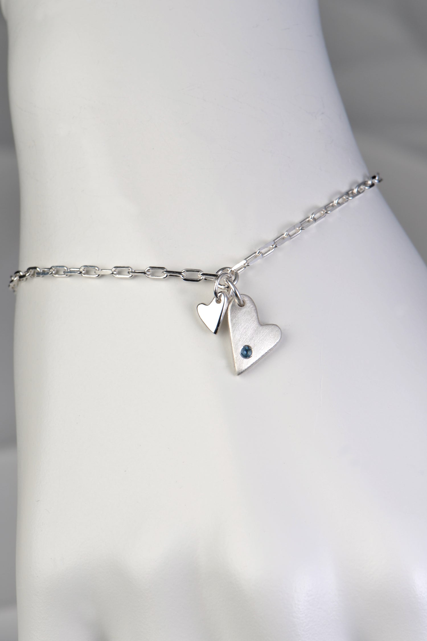 Sterling silver two‑heart bracelet with aquamarine displayed on white mannequin wrist to show size and scale from the From The Heart collection by Christine Sadler
