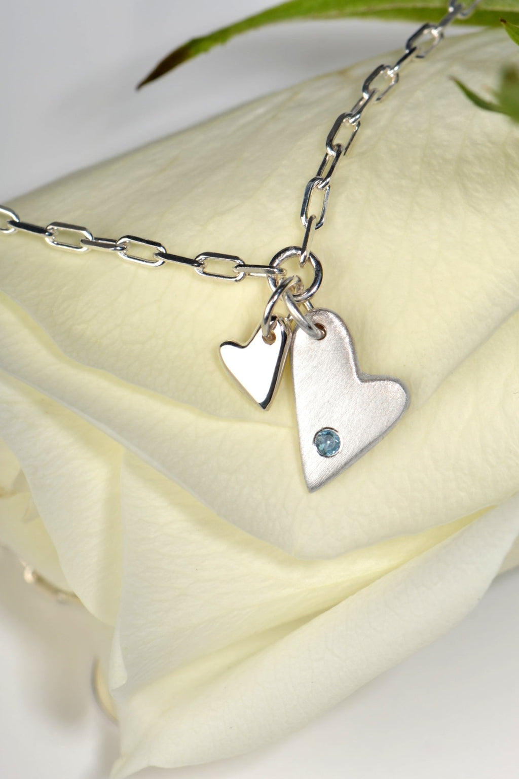 Sterling silver two‑heart bracelet with aquamarine displayed on white rose  from the From The Heart collection by Christine Sadler