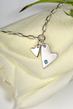 Sterling silver two‑heart bracelet with aquamarine displayed on white rose  from the From The Heart collection by Christine Sadler