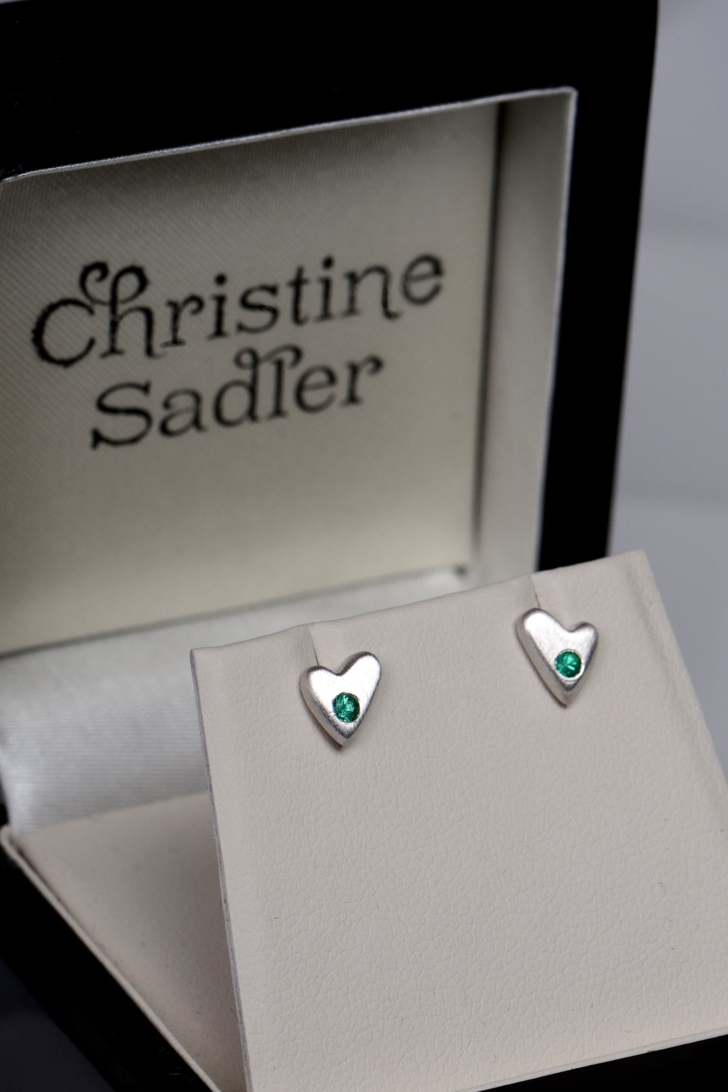 Handmade silver and Emerald heart earrings in a modern matt finish shown in a luxurious black and cream gift box that the earrings come gift wrapped in