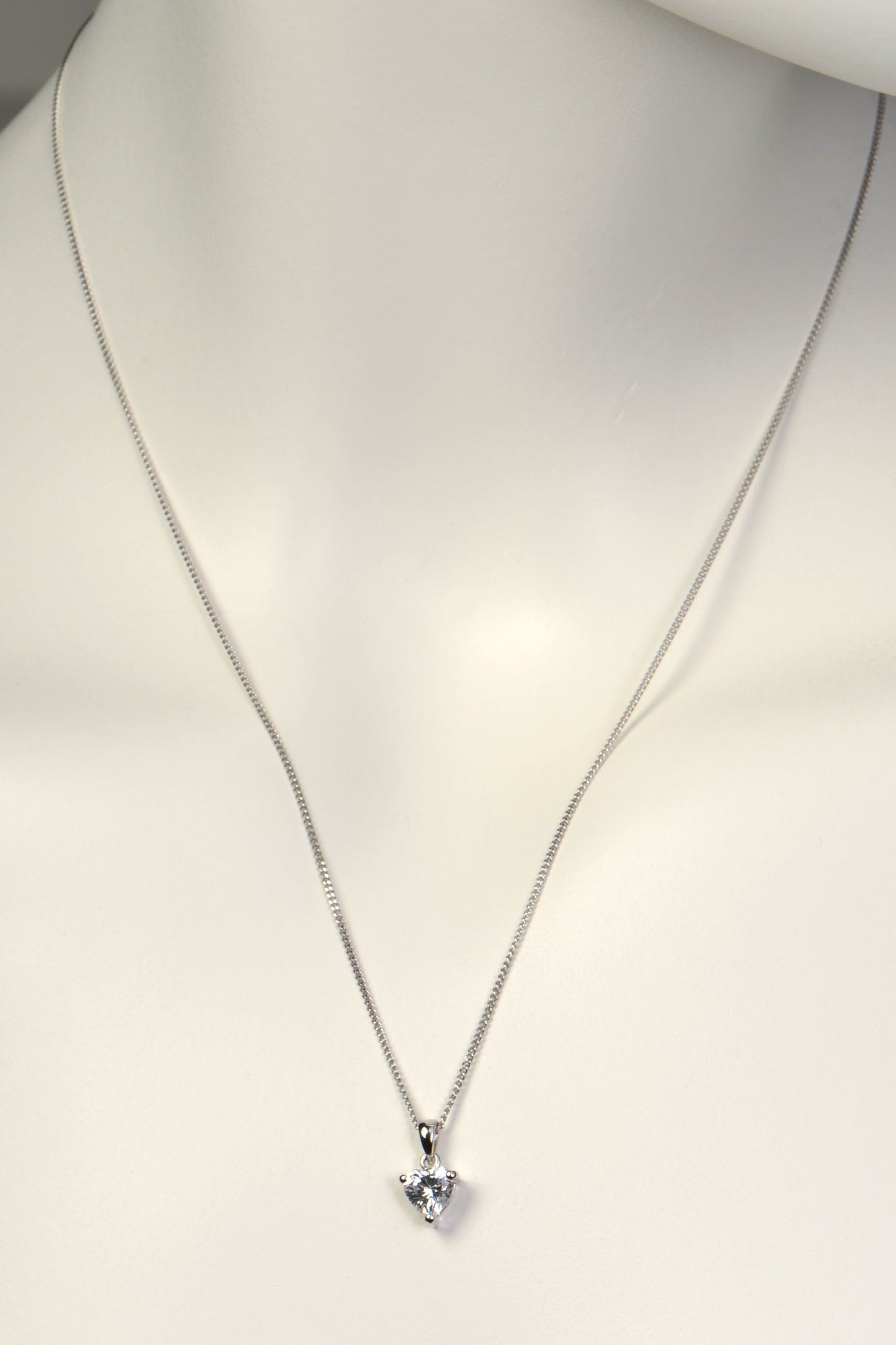 Silver necklace with a heart-shaped pendant on a mannequin.