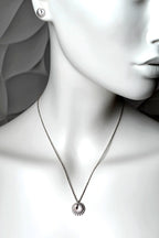 A sterling silver circular pendant necklace with a spoked wheel design, engraved "enough" displayed on a white mannequin bust. The mannequin also wears a matching round stud earring.