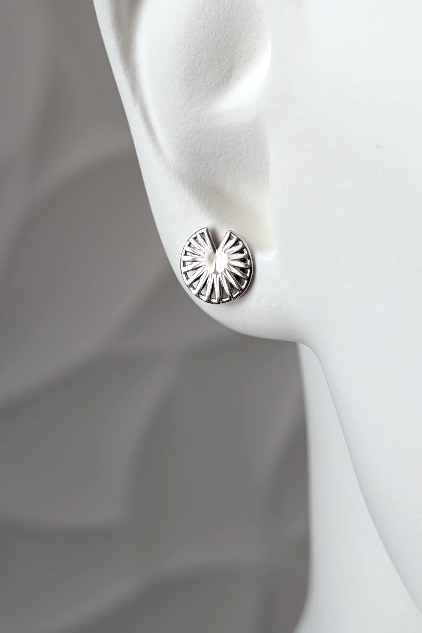 Sterling silver Break the Wheel talisman round stud earring shown on a mannequin ear to show size and scale