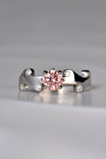 Large round pink lab diamond set in the middle of a platinum wavy ring with 6 small round white diamonds scattered across the front half of the band. This unique design by Christine Sadler is inspired by fire and the pink lab diamond is held by claws that are shaped into tiny flames. 