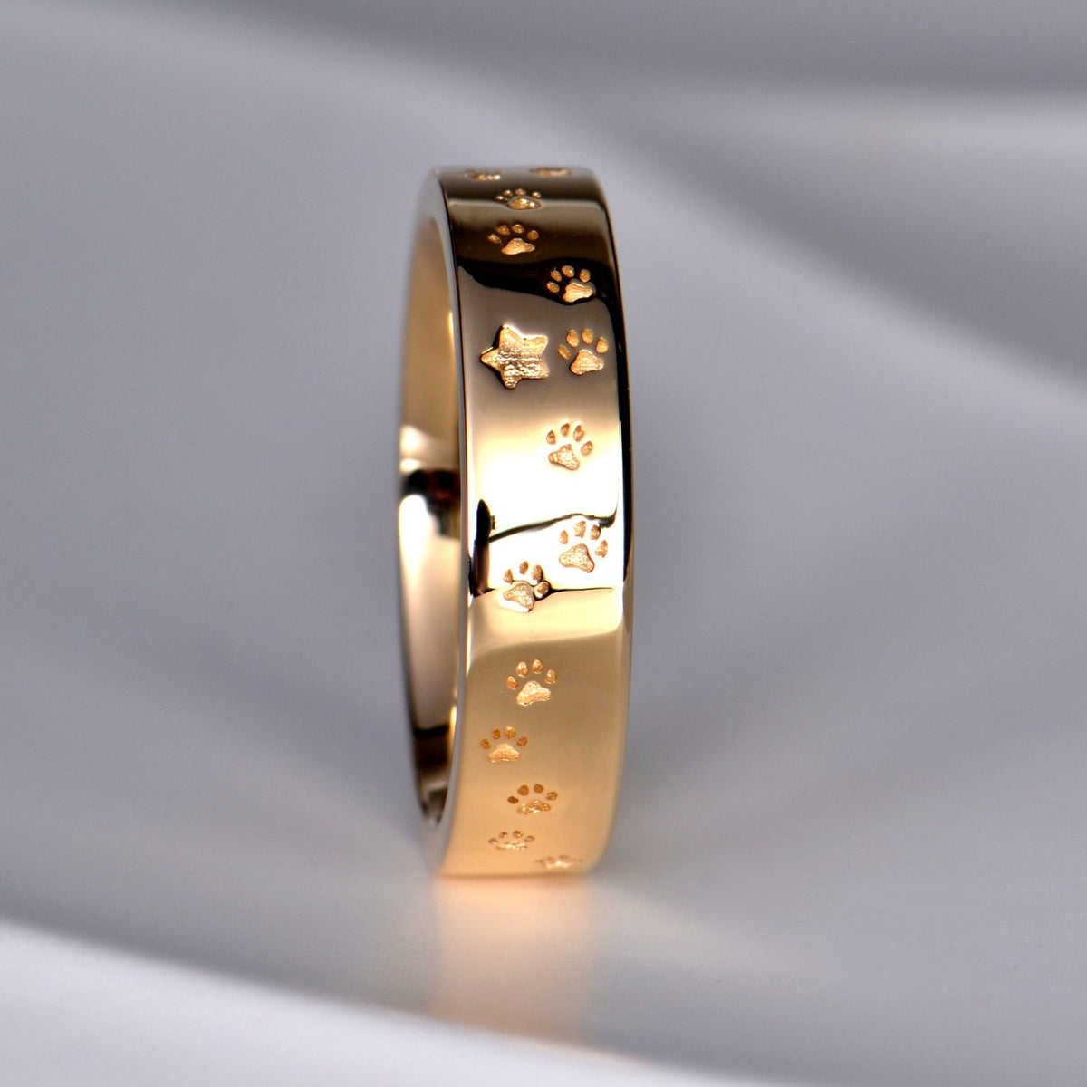 Custom yellow gold ring with paw print designs and stars on a gray background from Christine Sadler