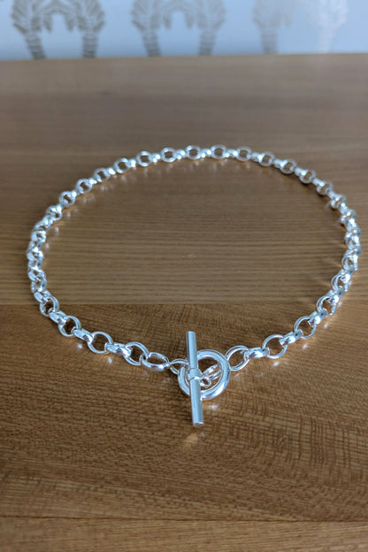 Sterling silver T-bar necklace with soldered links displayed on natural wood surface – secure and stylish design