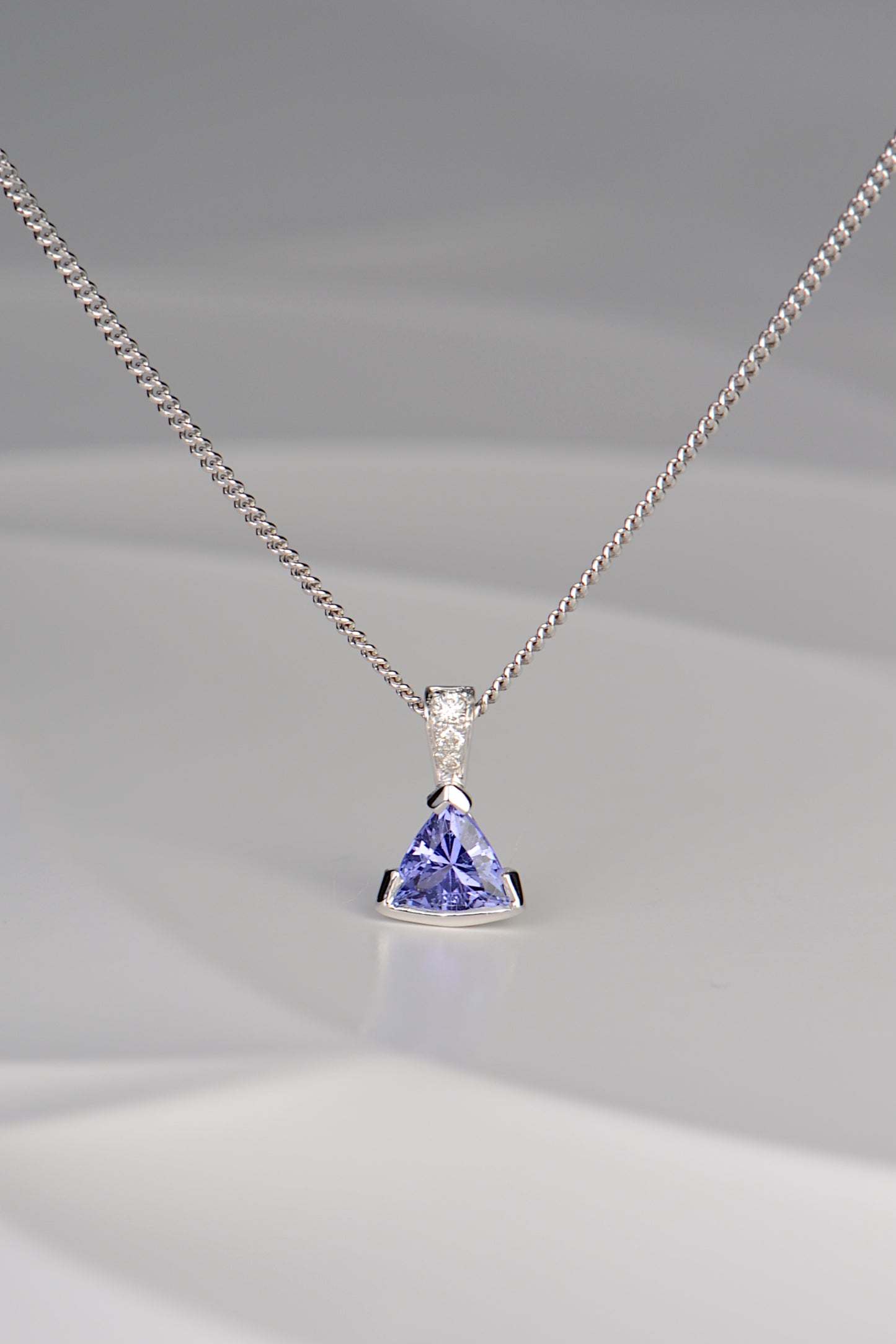 modern white gold necklace with three diamonds and a triangular tanzanite hanging below them by jewellery designer Christine Sadler