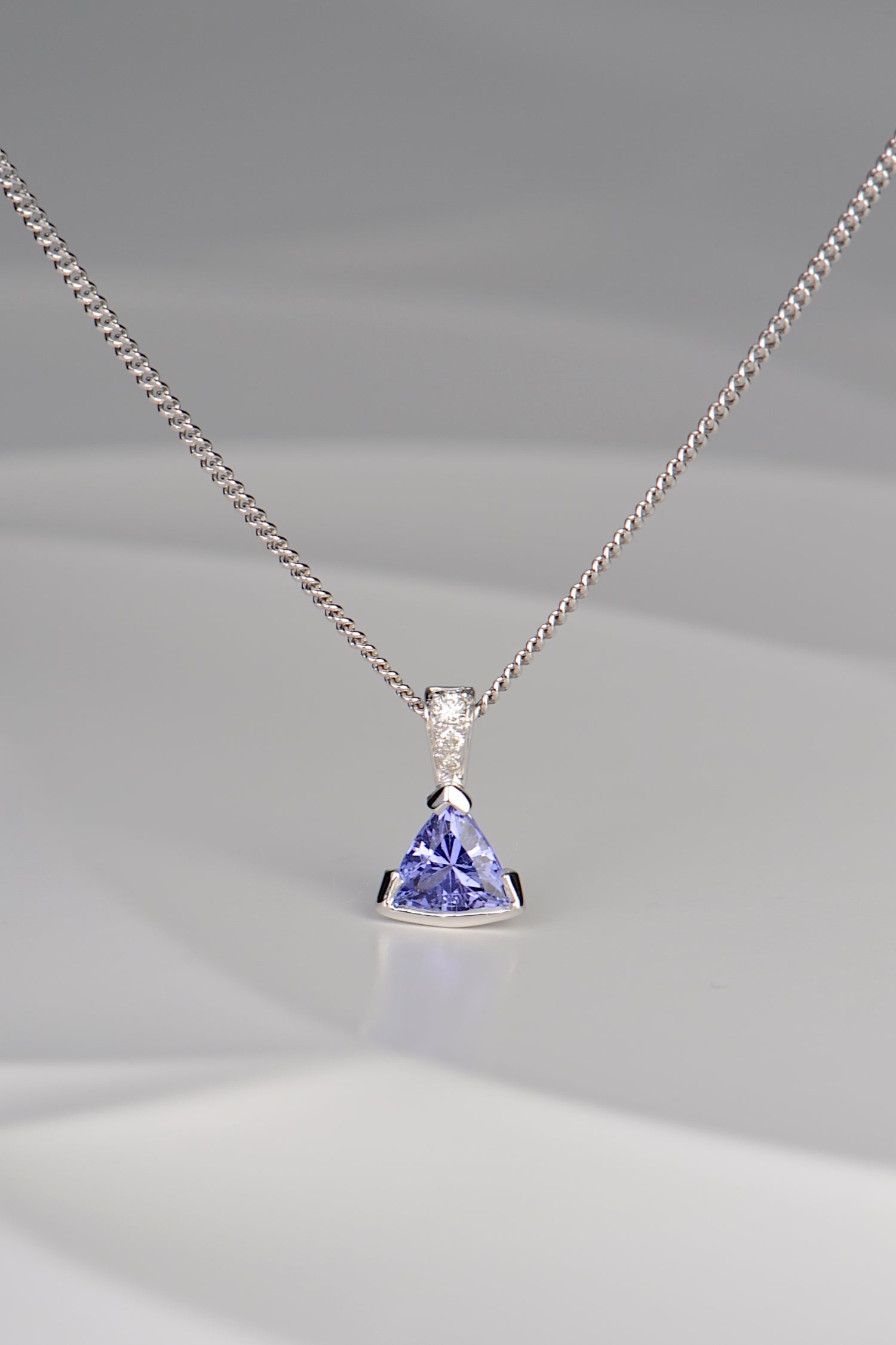 modern white gold necklace with three diamonds and a triangular tanzanite hanging below them by jewellery designer Christine Sadler