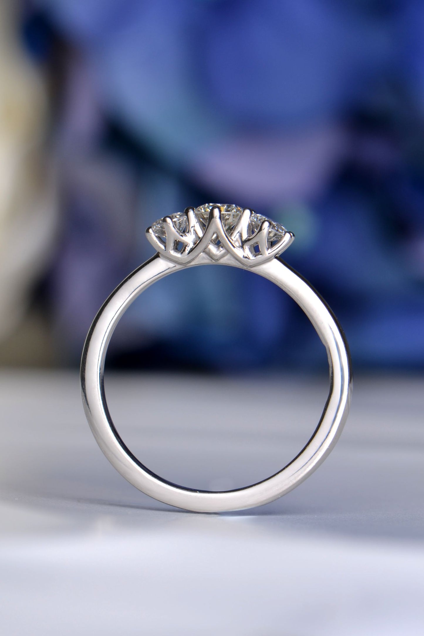Side profile of platinum cathedral engagement ring with criss-cross vaulted claw design holding three round diamonds