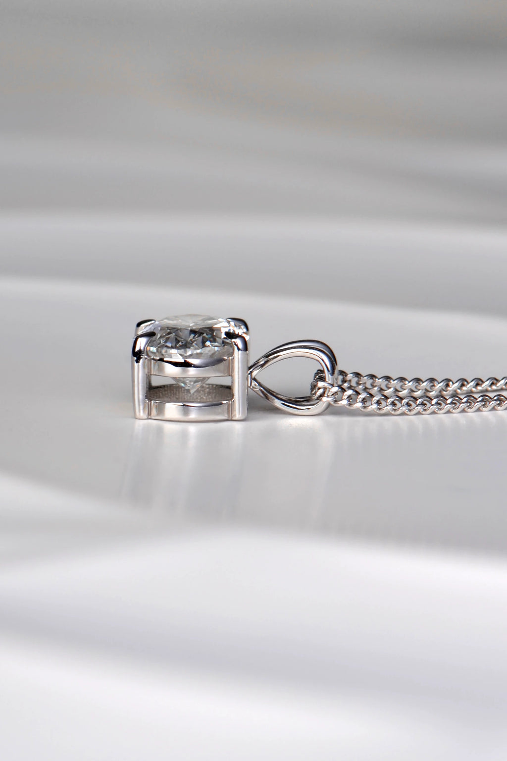 Side view of a white gold diamond pendant showing the double bail design, talon claws, and low-profile basket setting. Christine Sadler