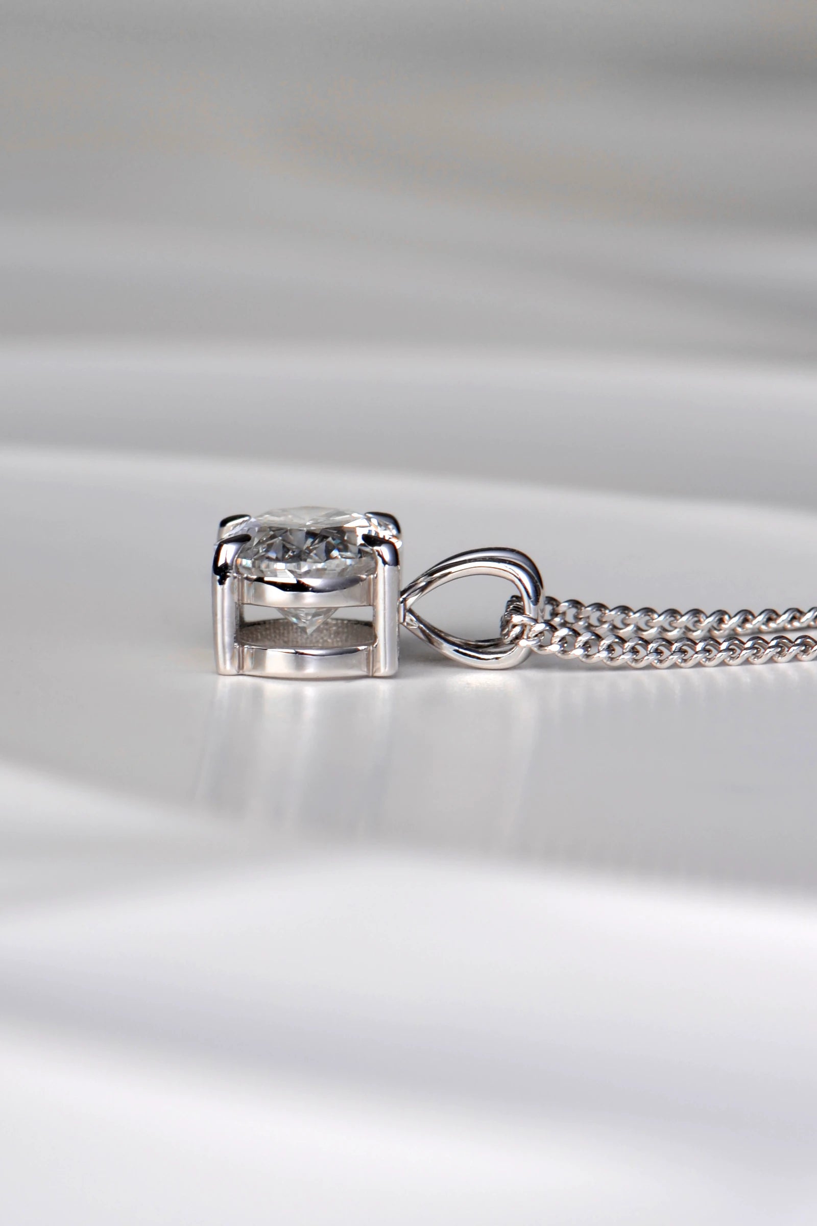 Side view of a white gold diamond pendant showing the double bail design, talon claws, and low-profile basket setting. Christine Sadler
