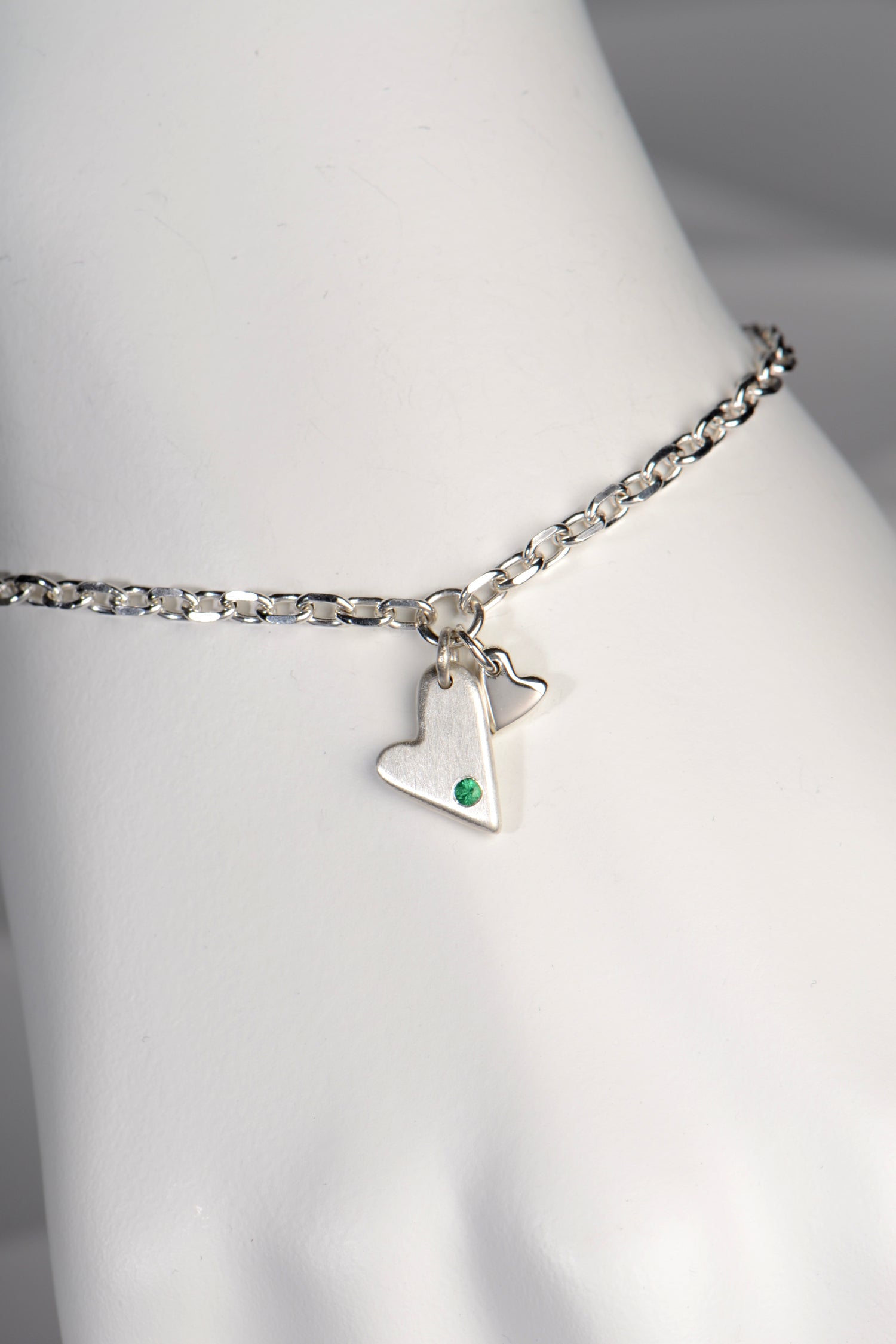 Sterling silver double heart bracelet set with emerald displayed on white mannequin wrist to show size and scale from the From The Heart collection by Christine Sadler