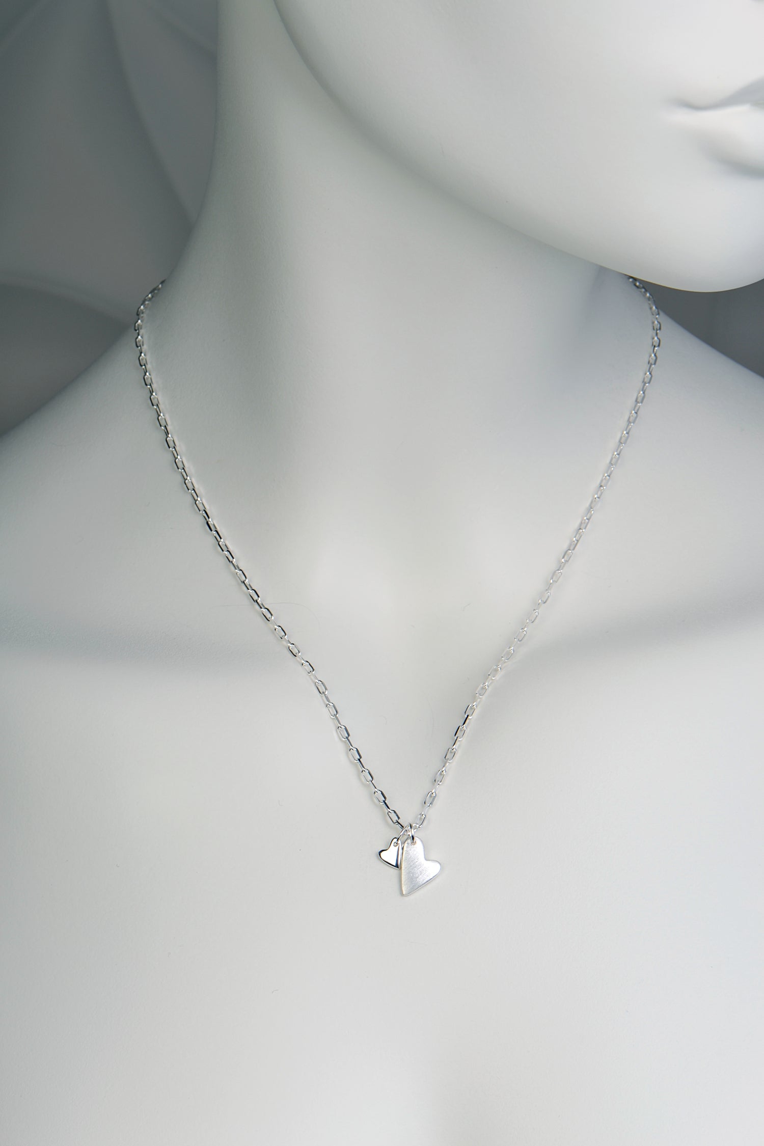 Sterling silver necklace with two heart pendants — one large matt heart and one small polished heart, From The Heart collection on white mannequin to show size and scale