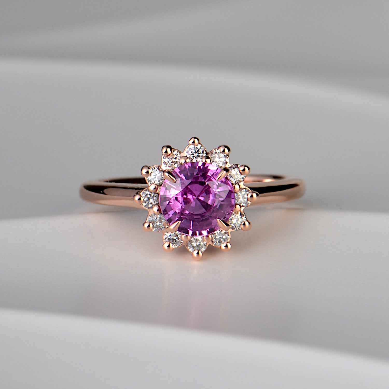 rose gold engagement ring with a large deep pink sapphire in the middle surrounded by twelve small diamonds in a flower - Christine Sadler