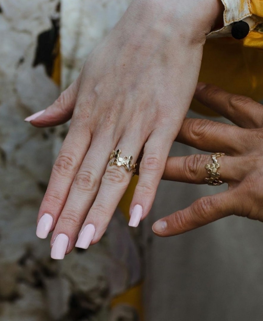 A couple's hands on their wedding day wearing Christine Sadler's unique honeycomb 18ct gold and platinum wedding rings that are shaped in a wide hexagonal honeycomb pattern with a tiny bee.