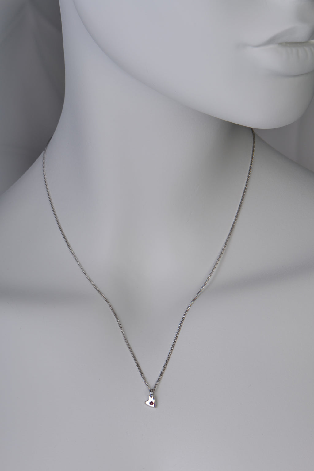 Small polished white gold heart necklace with a ruby displayed on white mannequin to show size and scale when on a 45cm long chain