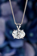 Close-up of a 2.06 carat oval lab-grown diamond pendant necklace in an East-West setting against a blurred blue hydrangea flower background. Christine Sadler