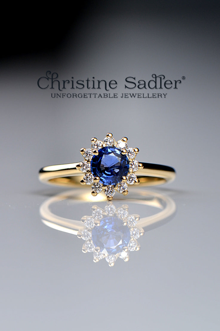 handcrafted 18ct yellow gold engagement ring with a large deep blue sapphire surrounded by twelve small wite diamonds in a flower shape - Chrisitne Sadler