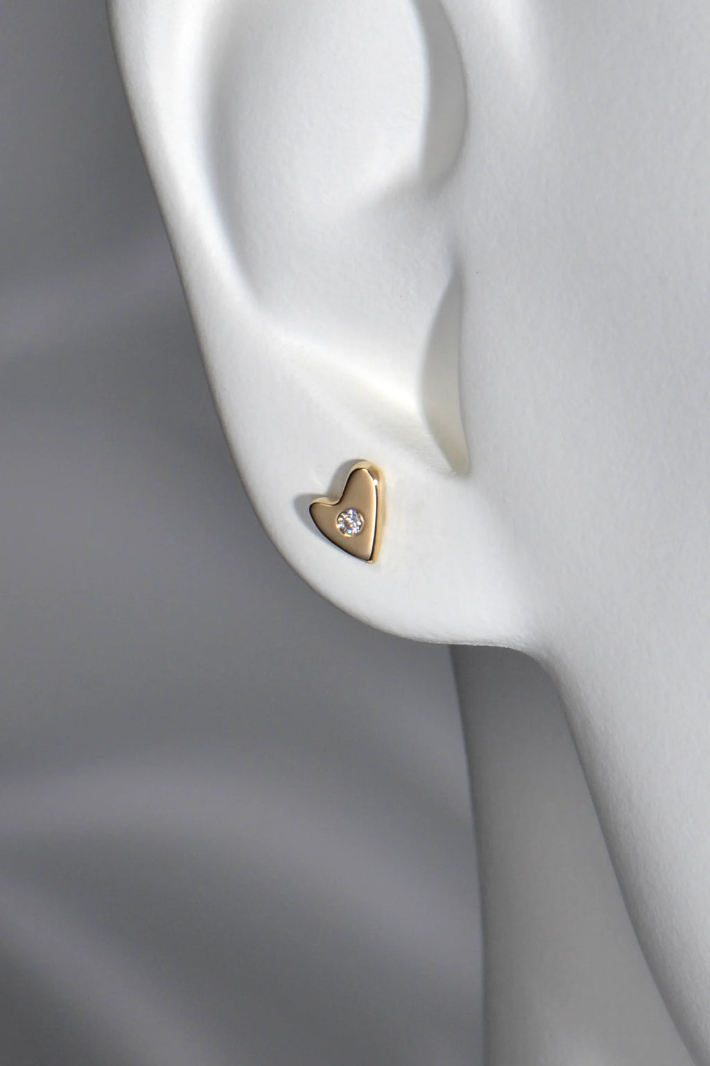9ct yellow gold heart stud earrings with flush-set diamonds in a mannequin ear to show size and scale.
