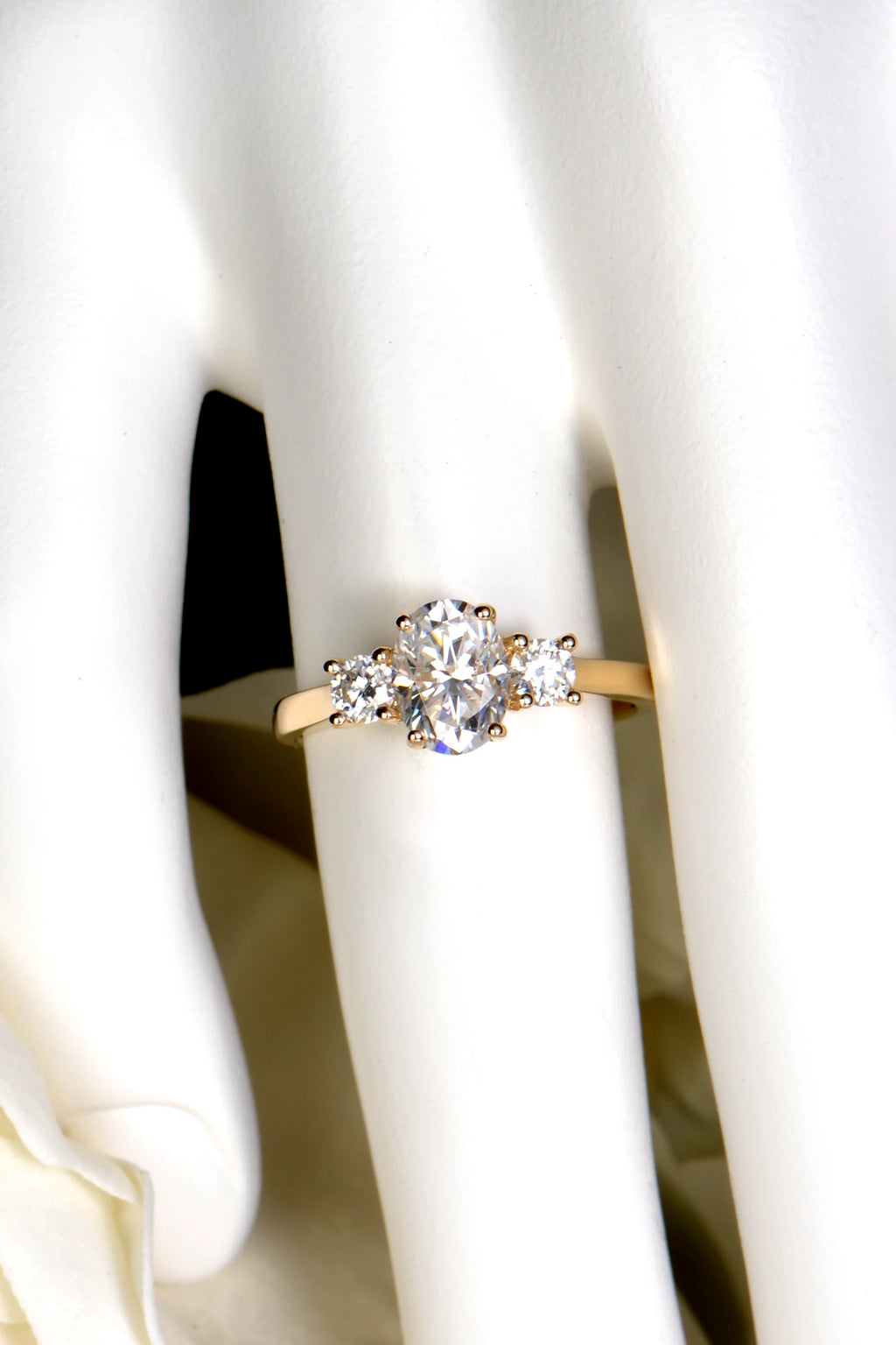 A 9ct yellow gold oval moissanite trilogy engagement ring being worn on a hand to demonstrate size, scale, and finger coverage.
