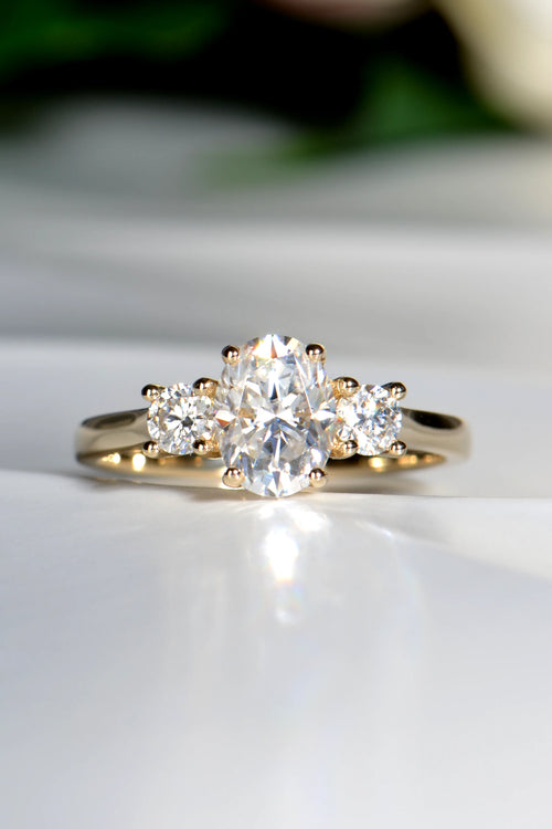 Handcrafted 9ct yellow gold trilogy engagement ring featuring a central oval moissanite stone flanked by two round brilliant cut side stones.