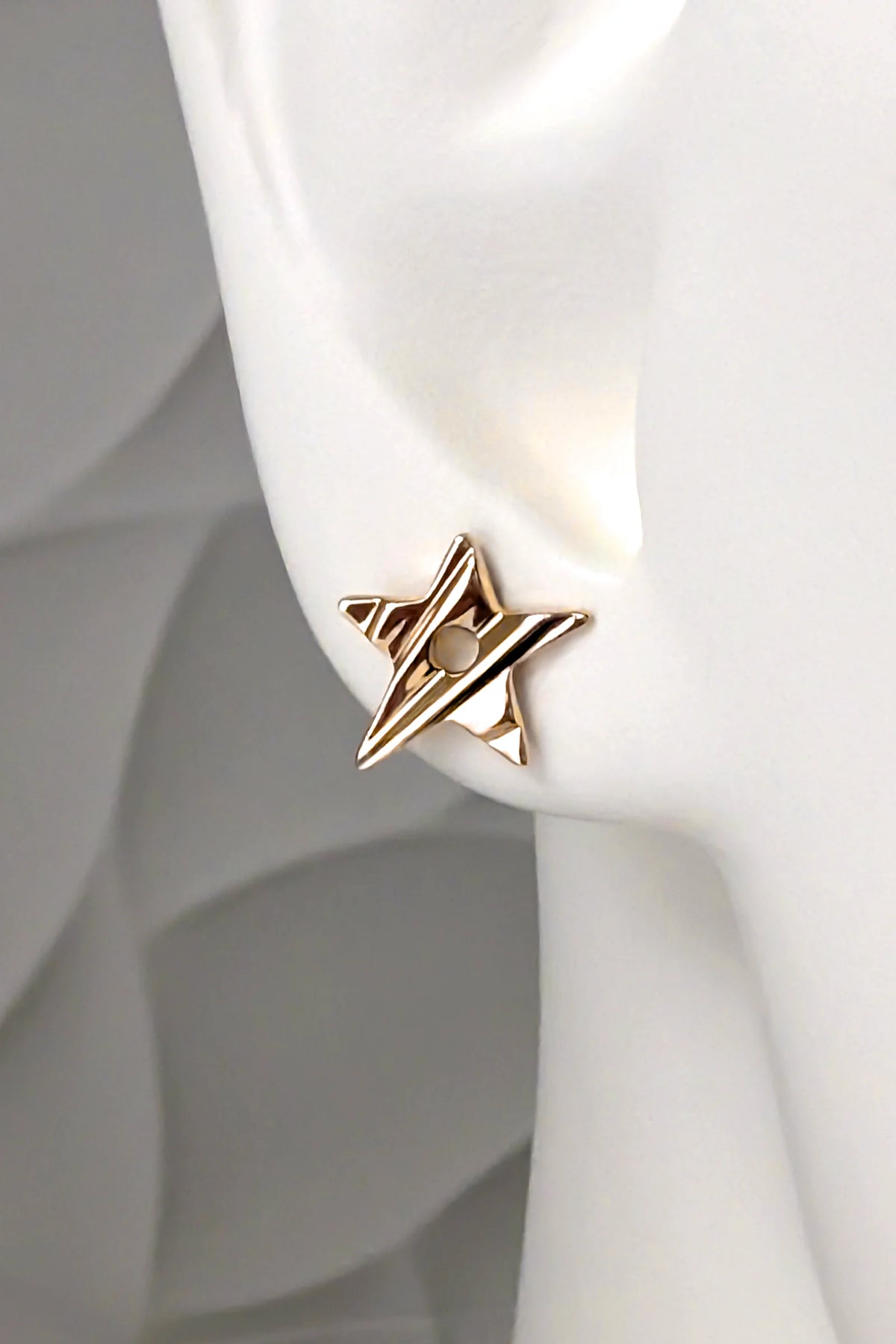 solid 9ct yellow gold star stud earring with a carved surface that catches the light and a circular hole in the middle, shown in a mannequin ear to demonstrate size and scale