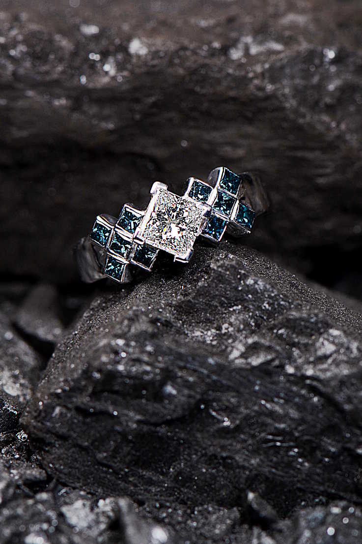 Diamond Tartan ring design by Christine Sadler sitting on pieces of coal. 