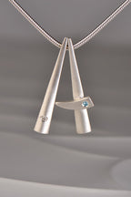two modern brushed finished silver pendants that stack together , one set with a diamond and one with a blue topaz. This exclusive collection of jewellery is called Cairn and you can stack different gemstones together to mark important moments in your personal journey from Scottish jewellery designer Christine Sadler