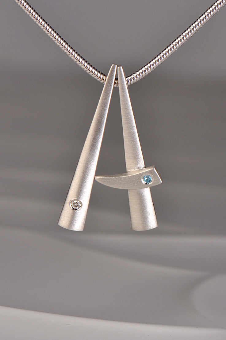 two modern brushed finished silver pendants that stack together , one set with a diamond and one with a blue topaz. This exclusive collection of jewellery is called Cairn and you can stack different gemstones together to mark important moments in your personal journey from Scottish jewellery designer Christine Sadler