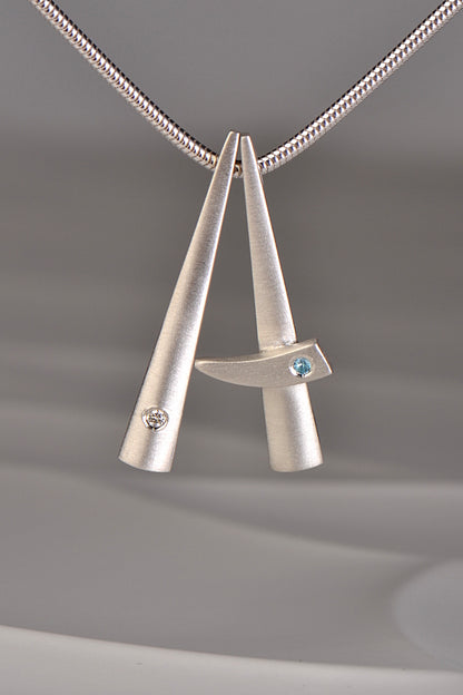 two modern brushed finished silver pendants that stack together , one set with a diamond and one with a blue topaz. This exclusive collection of jewellery is called Cairn and you can stack different gemstones together to mark important moments in your personal journey from Scottish jewellery designer Christine Sadler
