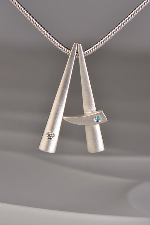 two modern brushed finished silver pendants that stack together , one set with a diamond and one with a blue topaz. This exclusive collection of jewellery is called Cairn and you can stack different gemstones together to mark important moments in your personal journey from Scottish jewellery designer Christine Sadler