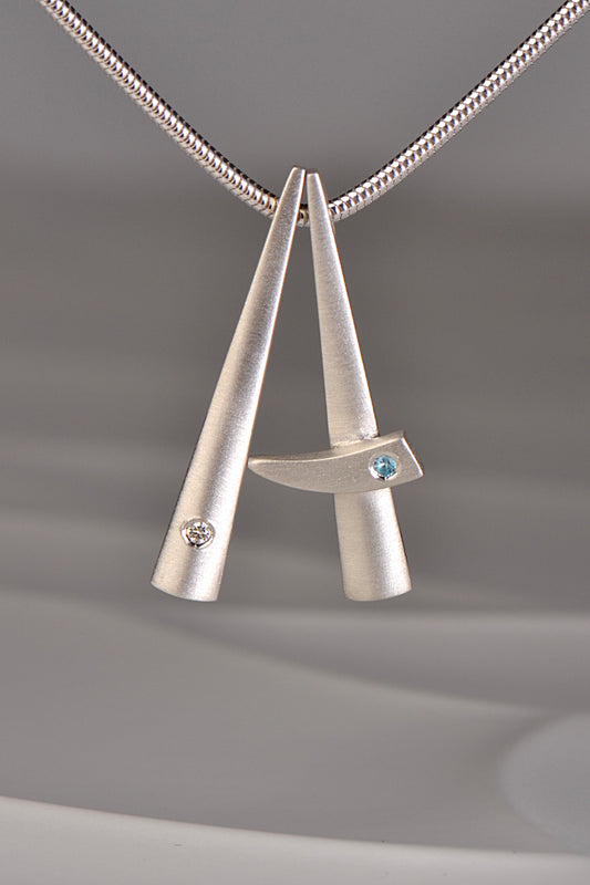 two modern brushed finished silver pendants that stack together , one set with a diamond and one with a blue topaz. This exclusive collection of jewellery is called Cairn and you can stack different gemstones together to mark important moments in your personal journey from Scottish jewellery designer Christine Sadler