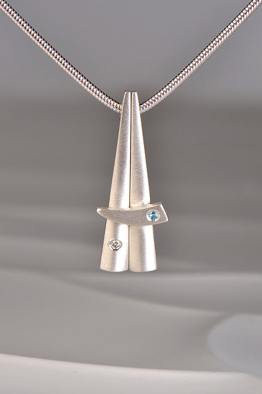 contemporary stacking pendants in brushed sterling silver that are inspired by Scottish Cairns by Christine Sadler. One is set with a diamond and the other with a blue topaz.