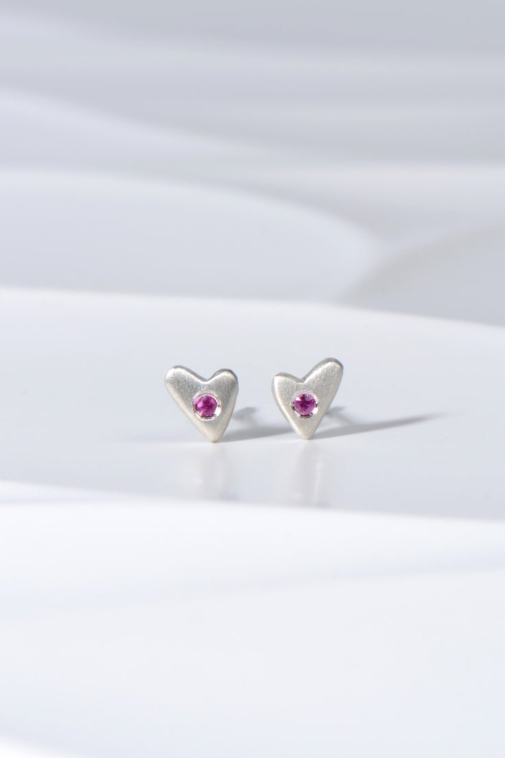 Small matt silver heart stud earrings set with pink sapphires displayed on white background from the From The Heart collection by Christine Sadler