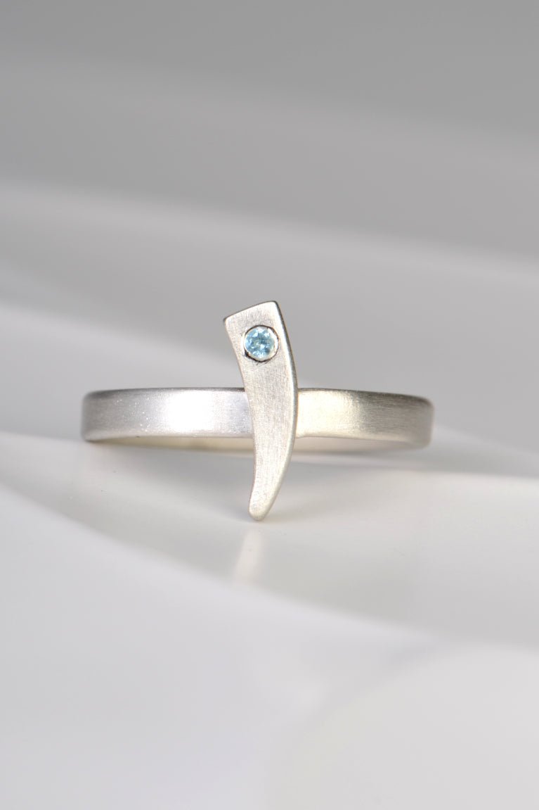 matt silver ring with a curved detail on top that sits at right angles to the band. The curve is set with a blue topaz from UK jewellery designer Christine Sadler