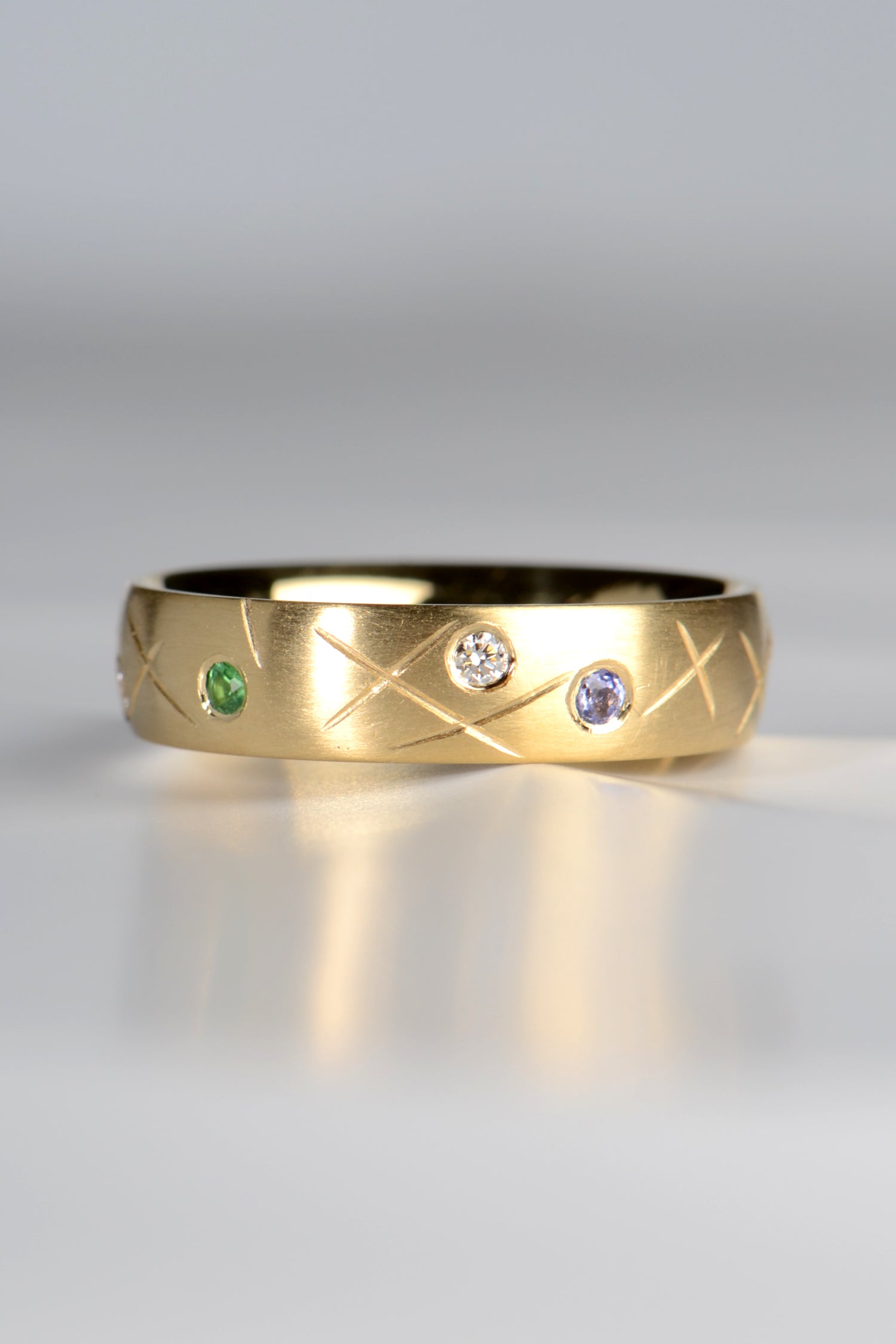 18ct yellow gold ring set with a green garent a diamond and a tanzanite with a criss cross pattern between the stones, inspired by sprinkles and designed by Christine Sadler to evoke happy memories