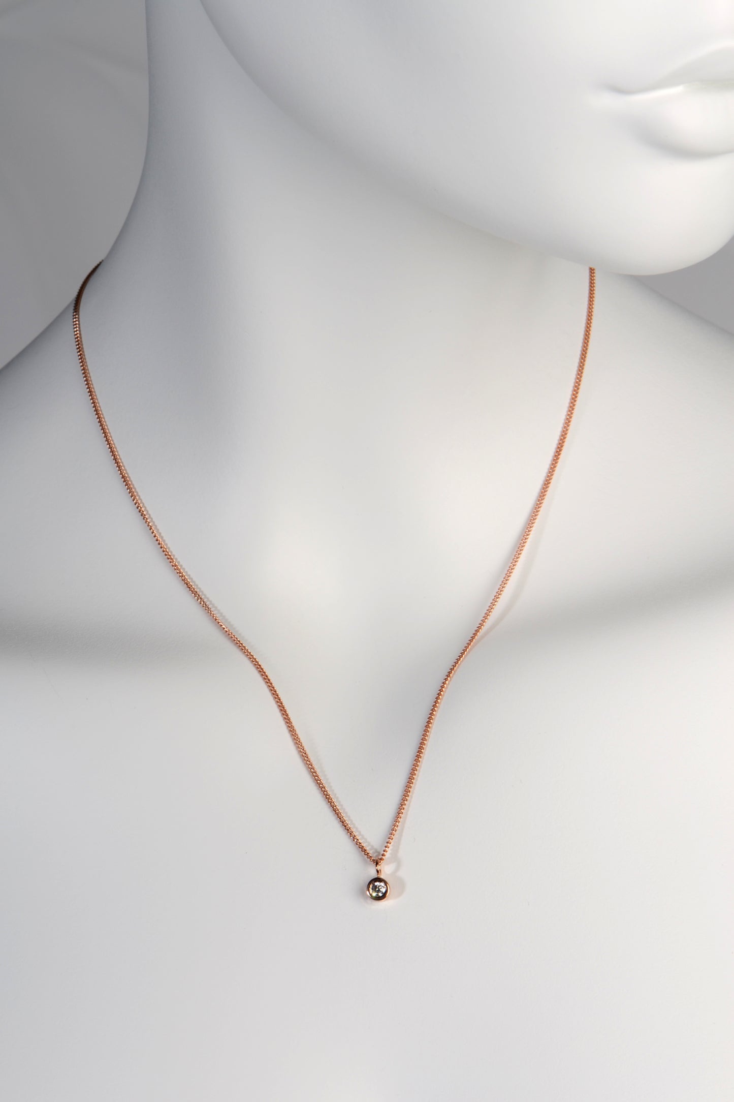 Petite diamond necklace made in 9ct rose gold. A small solid circle of rose gold 5mm in diameter hangs on a 45cm long rose gold curb chain. The diamond is 0.10ct G colour VS clarity. 
