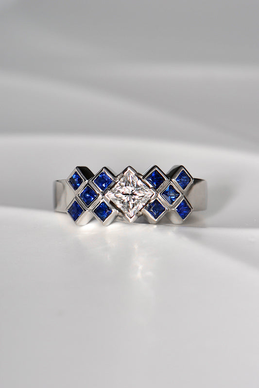 Princess cut diamond ring set with square blue sapphires in a tartan pattern. The ring is made of platinum and is a unique copyrighted design. 