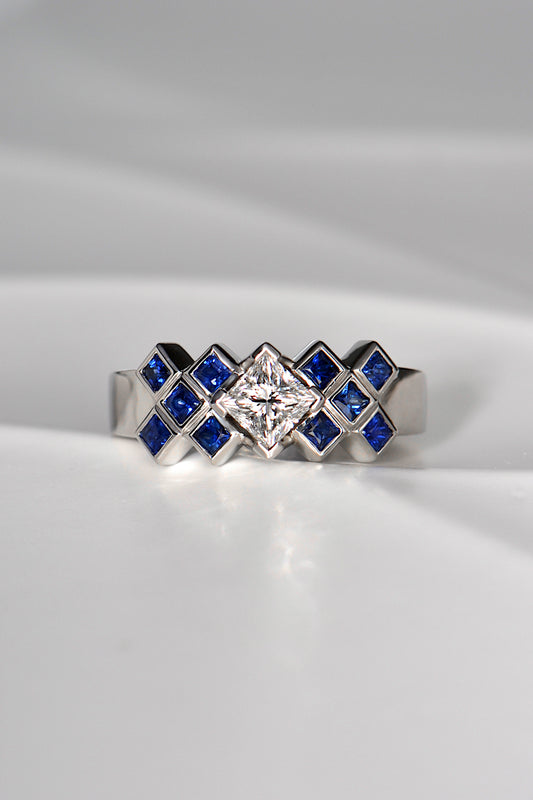 Princess cut diamond ring set with square blue sapphires in a tartan pattern. This Scottish ring is made of platinum and is a unique copyrighted design. 