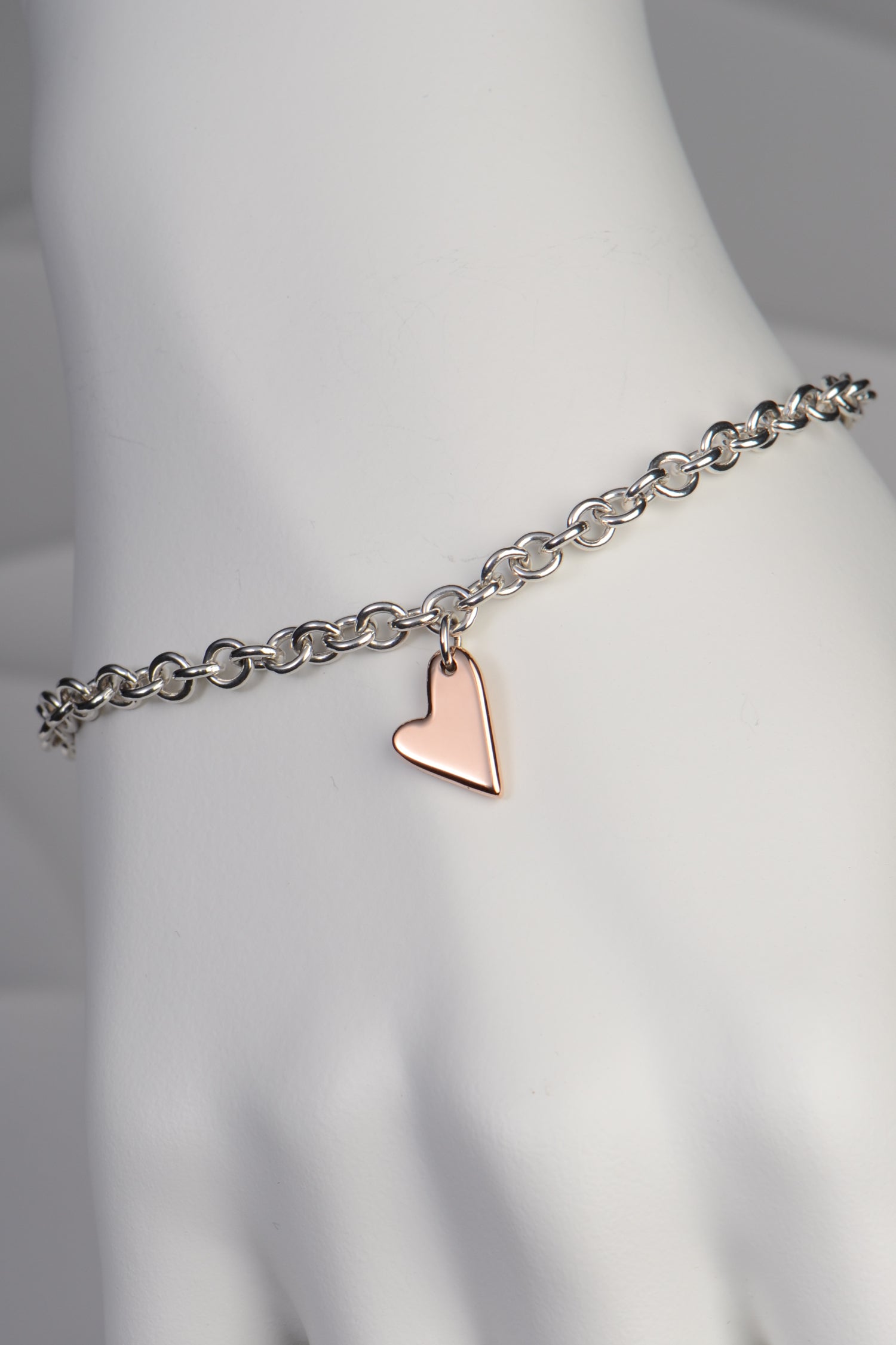 detail of Sterling silver bracelet with two highly polished 9ct rose gold hearts showing the large heart at the front on a white mannequin hand to show size and scale - From The Heart collection